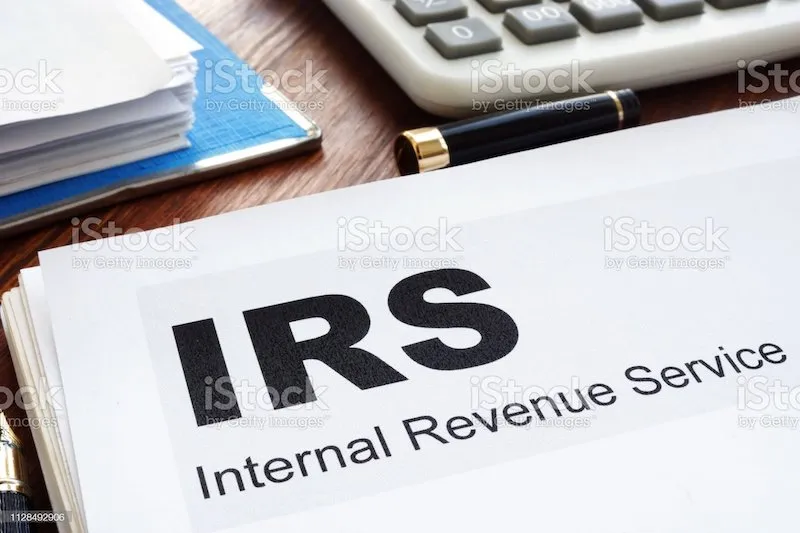 Paper with IRS internal revenue service typed on it with a calculator and pen cap.