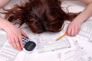 Woman laying on her debt bills with a calculator feeling overwhelmed. 