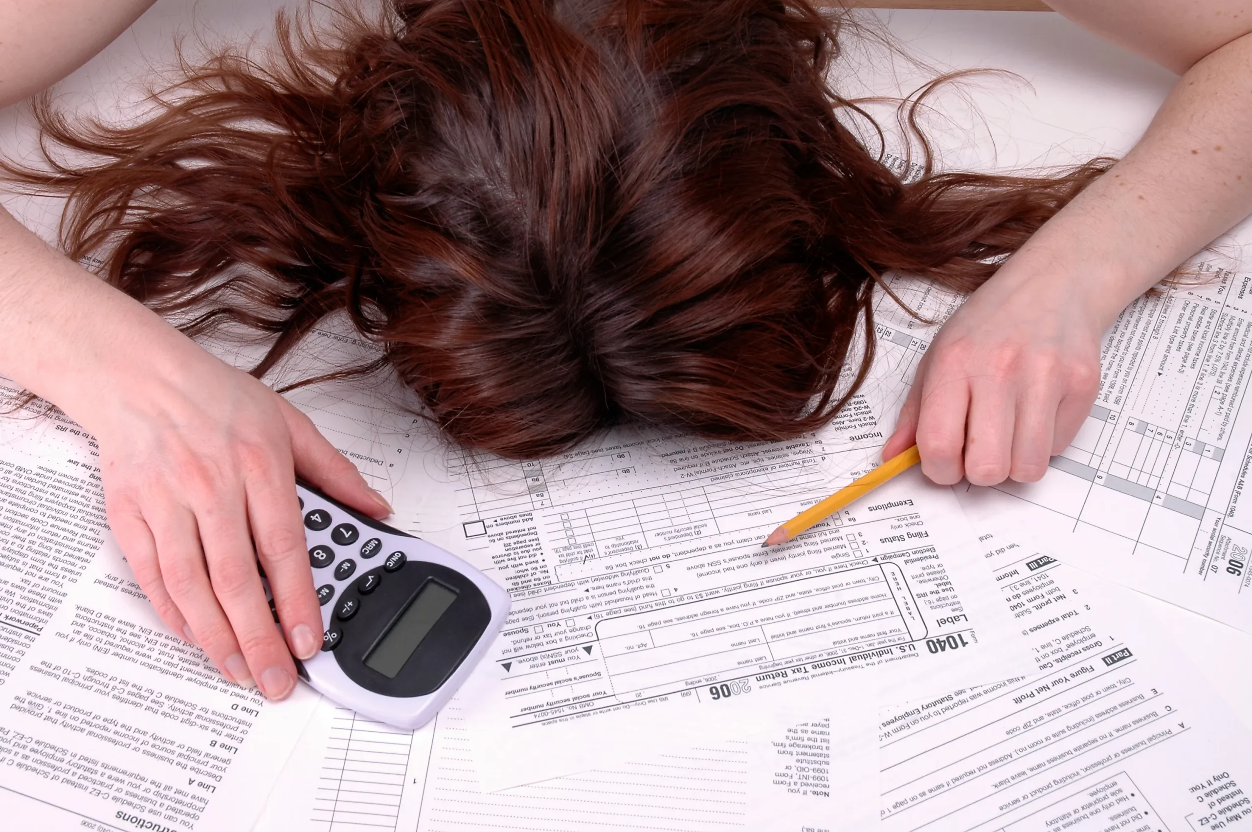 Woman laying on her debt bills with a calculator feeling overwhelmed.