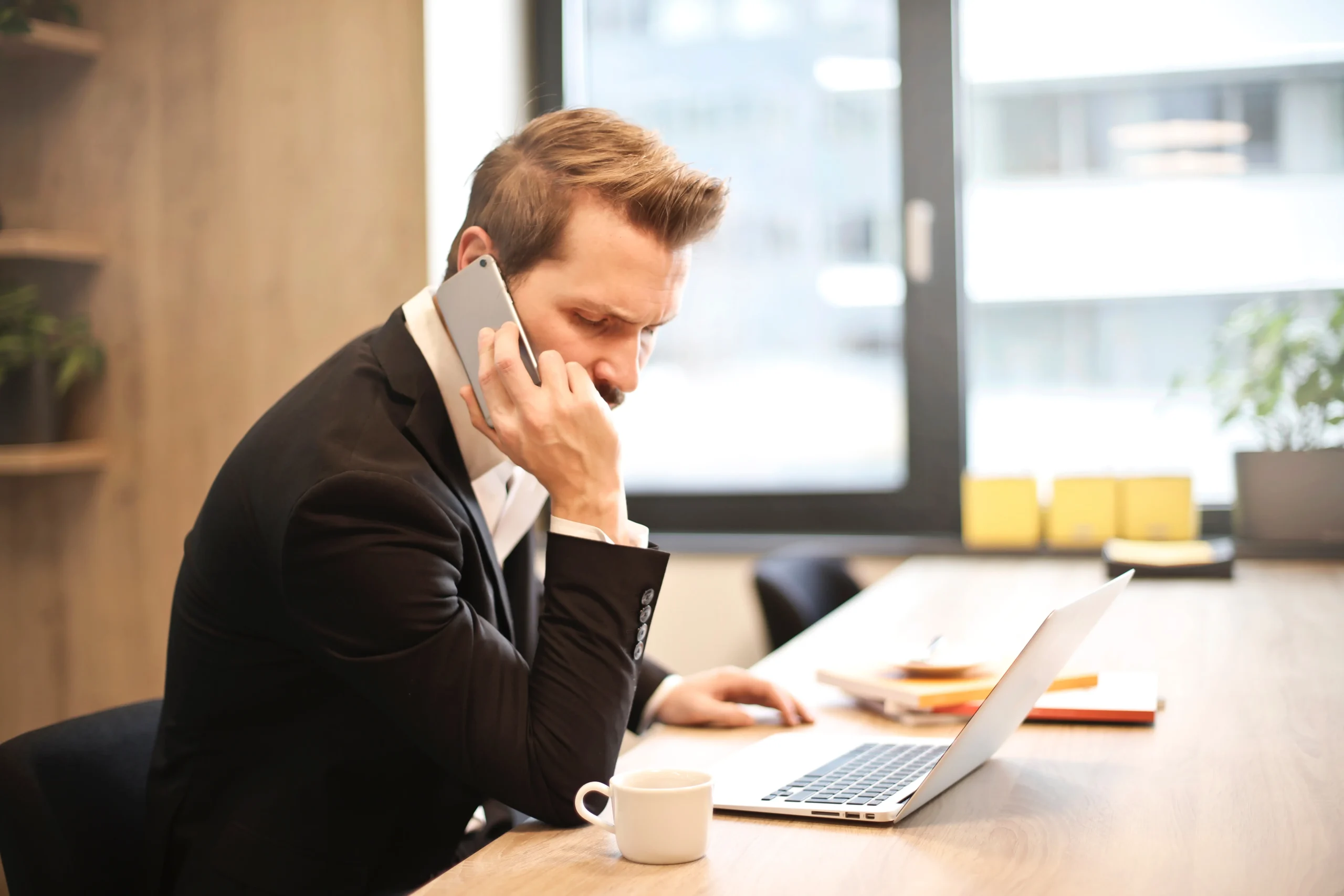 Man at his desk with computer and coffee. He is on the phone with the IRS and looks very angry. He needs to contact an Austin IRS defense lawyer.