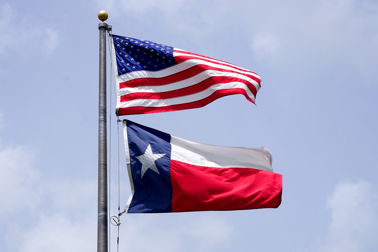 texas and american flag together on a flag pole.