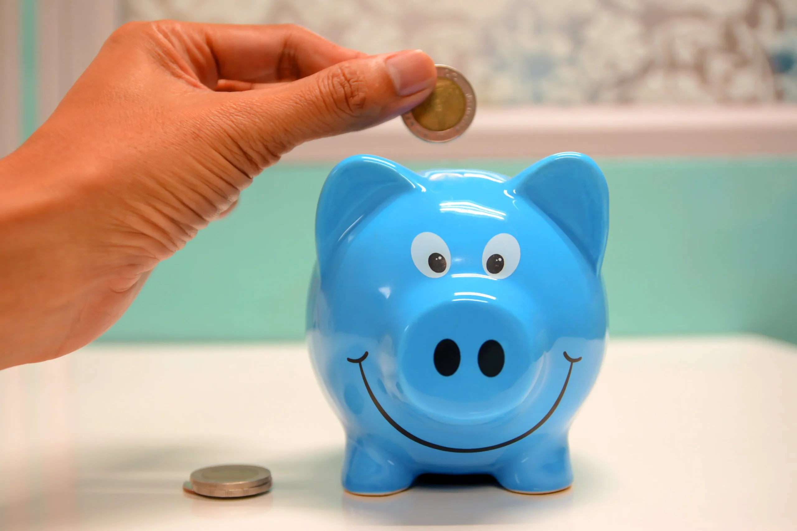 Someone putting a coin in a blue piggy bank.