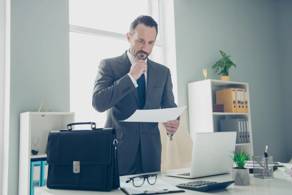 A man standing at his desk looking at a piece of paper.